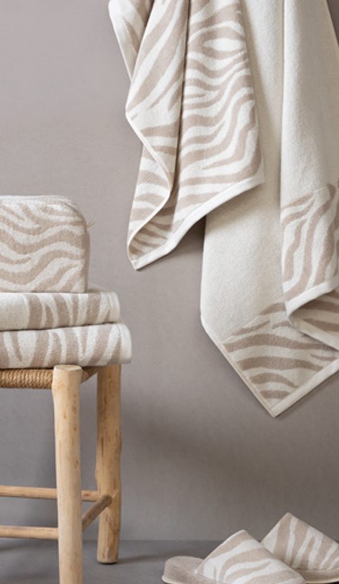Mantas y toallas de estilo zebra en tonos beige sobre una silla de madera.