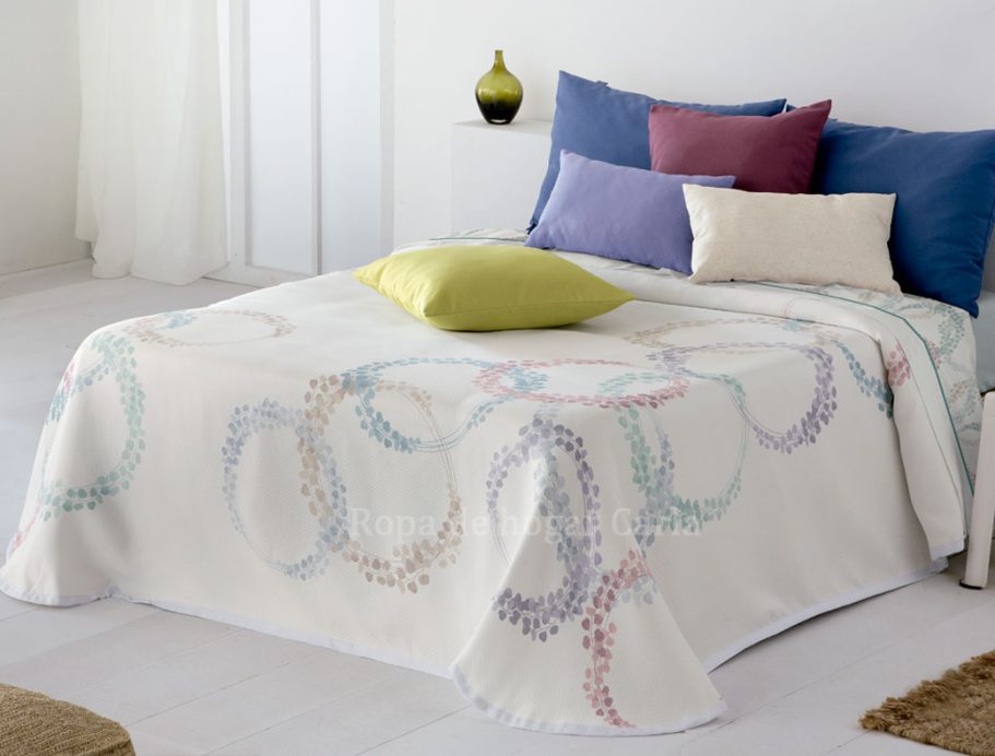 Colcha blanca con patrones de círculos y cojines de colores sobre una cama.