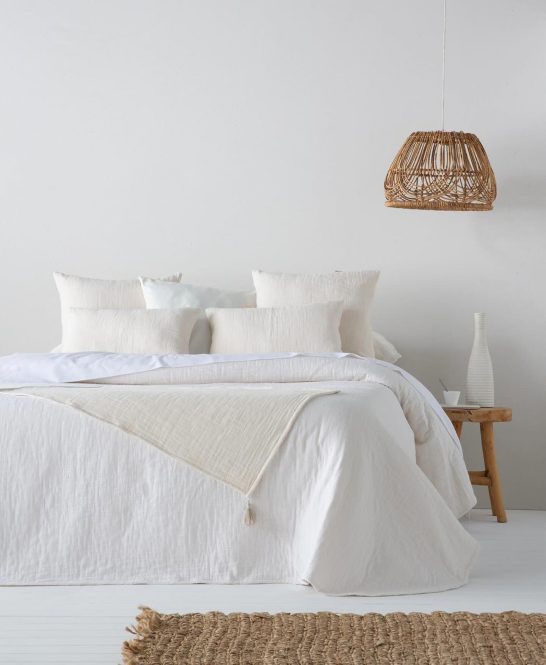 Cama con ropa de cama blanca y accesorios en un ambiente minimalista y luminoso.