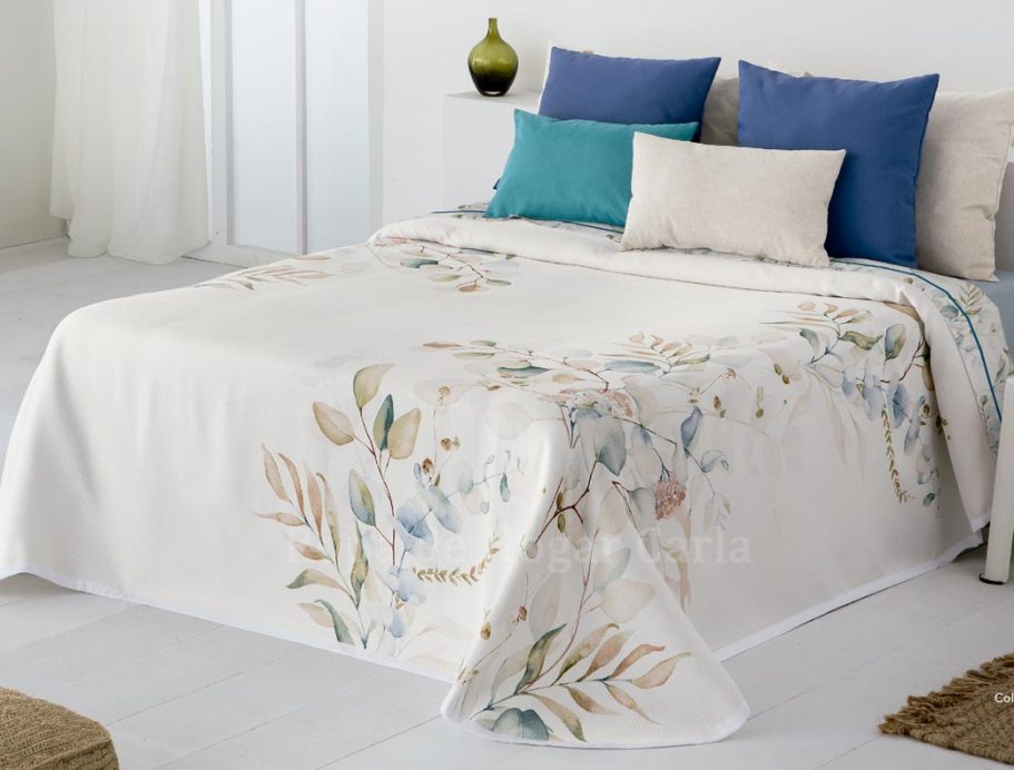 Cama con colcha blanca decorada con hojas y cojines azules y beige.