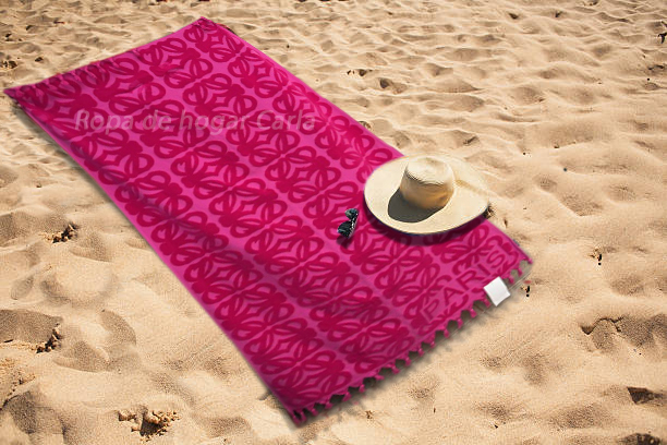 Toalla rosa sobre la arena con un sombrero y unas gafas de sol.