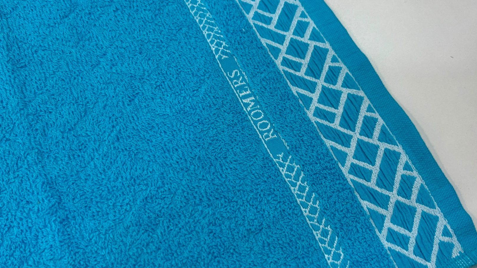 Toalla de color azul con un diseño decorativo en blanco en uno de sus bordes.
