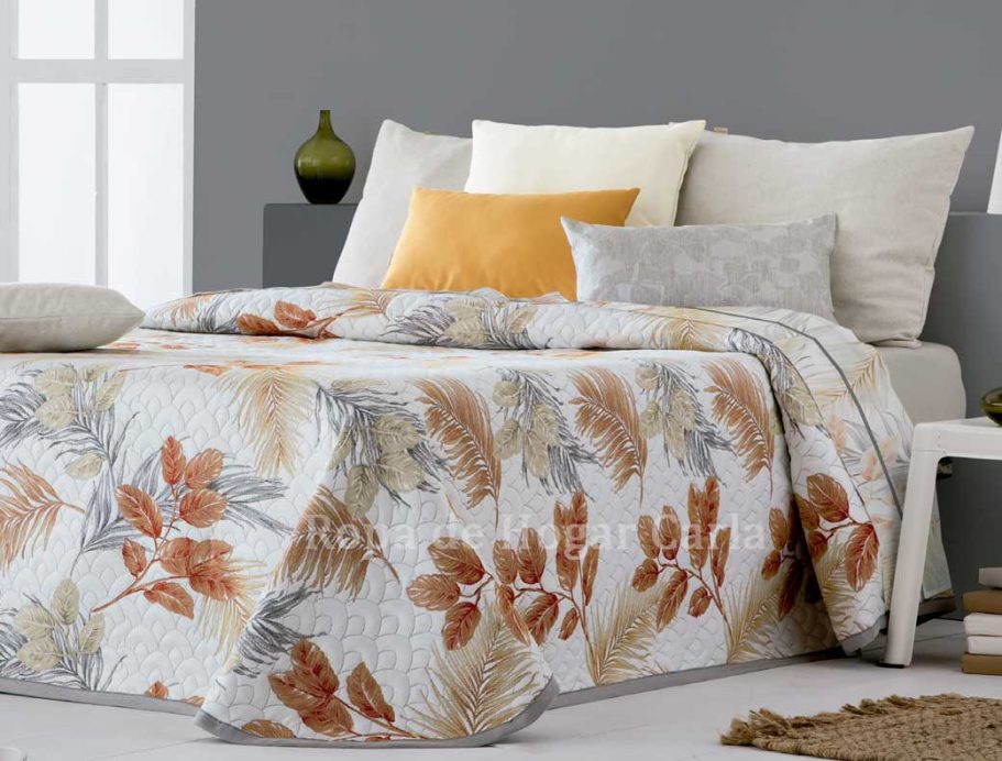 Colcha con motivos florales en tonos naranjas y amarillos sobre una cama decorada.