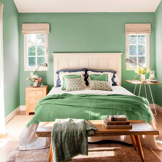 Habitación acogedora con paredes verdes, cama blanca y accesorios en tonos verdes y madera.