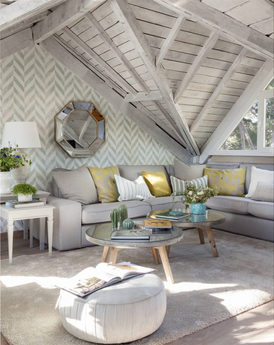 Salón moderno con techo inclinado, muebles claros y decoración en tonos suaves.