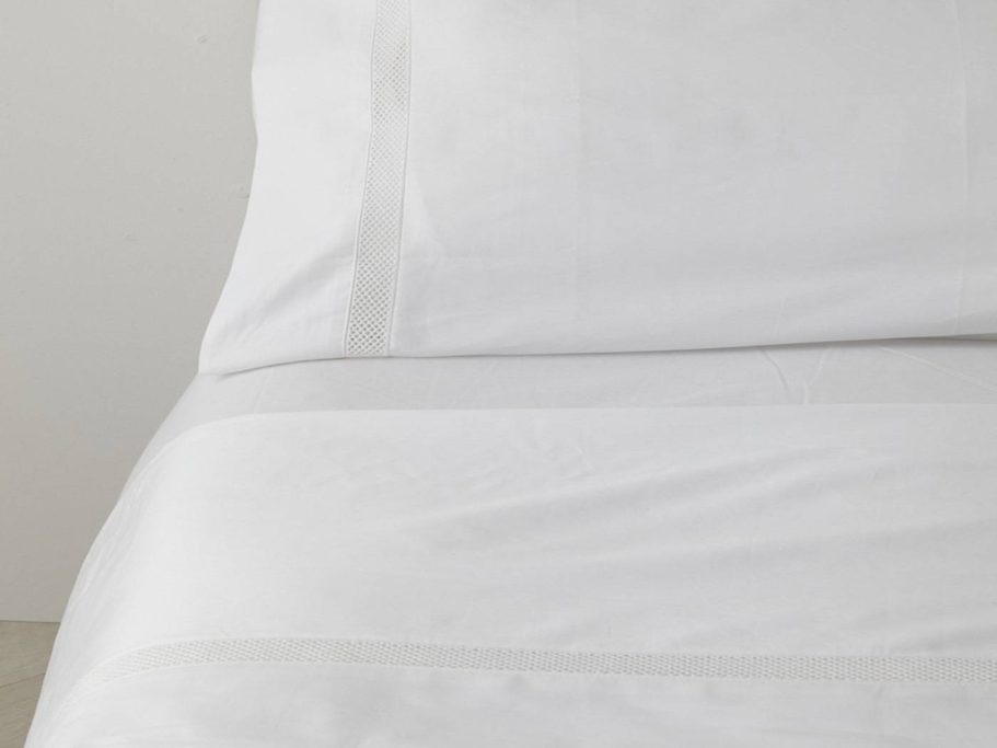 Juego de cama blanco con cojines decorativos en una cama moderna.