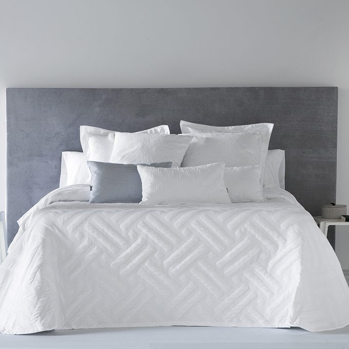 Edredón de cama blanco sobre una cama con almohadas y una mesita de noche.