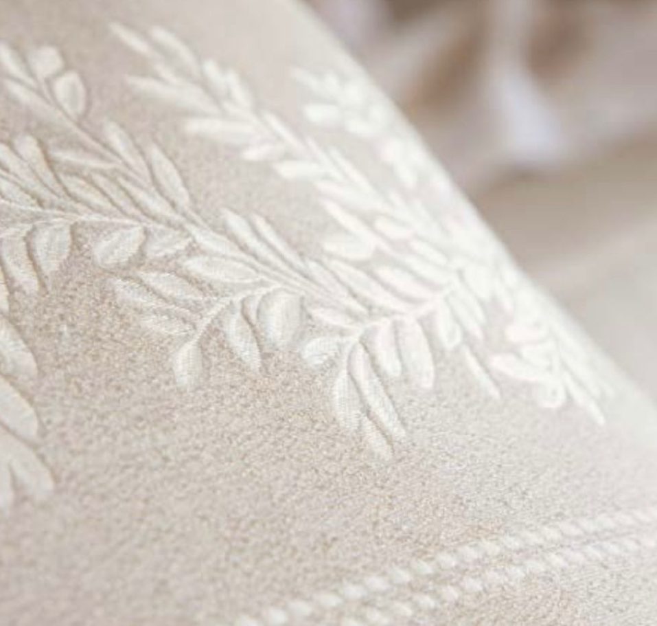 Detalle de un tejido beige con bordados de hojas en relieve.