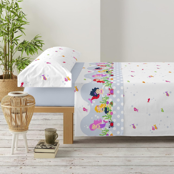 Colcha blanca con estampado colorido de personajes y flores sobre una cama de madera.