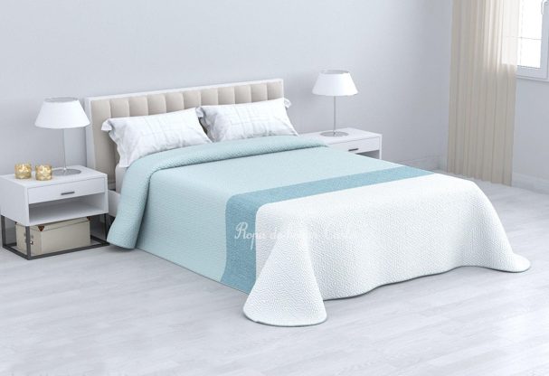 Cama con colcha azul claro y blanca, mesitas de noche y lámparas en una habitación clara.