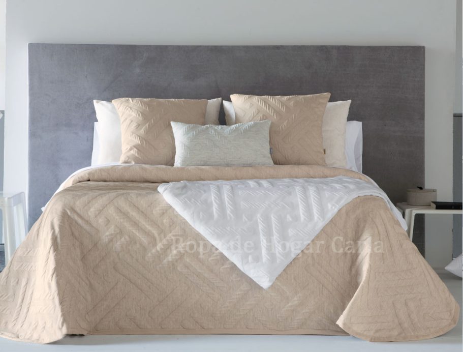 Cama con edredón beige, almohadas blancas y una manta blanca en un ambiente moderno.