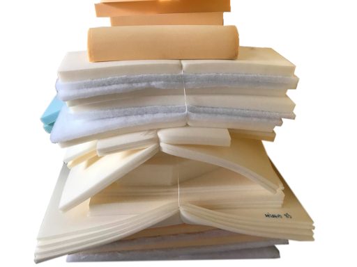 Varios bloques y hojas de espuma apilados, en tonos beige y blanco.