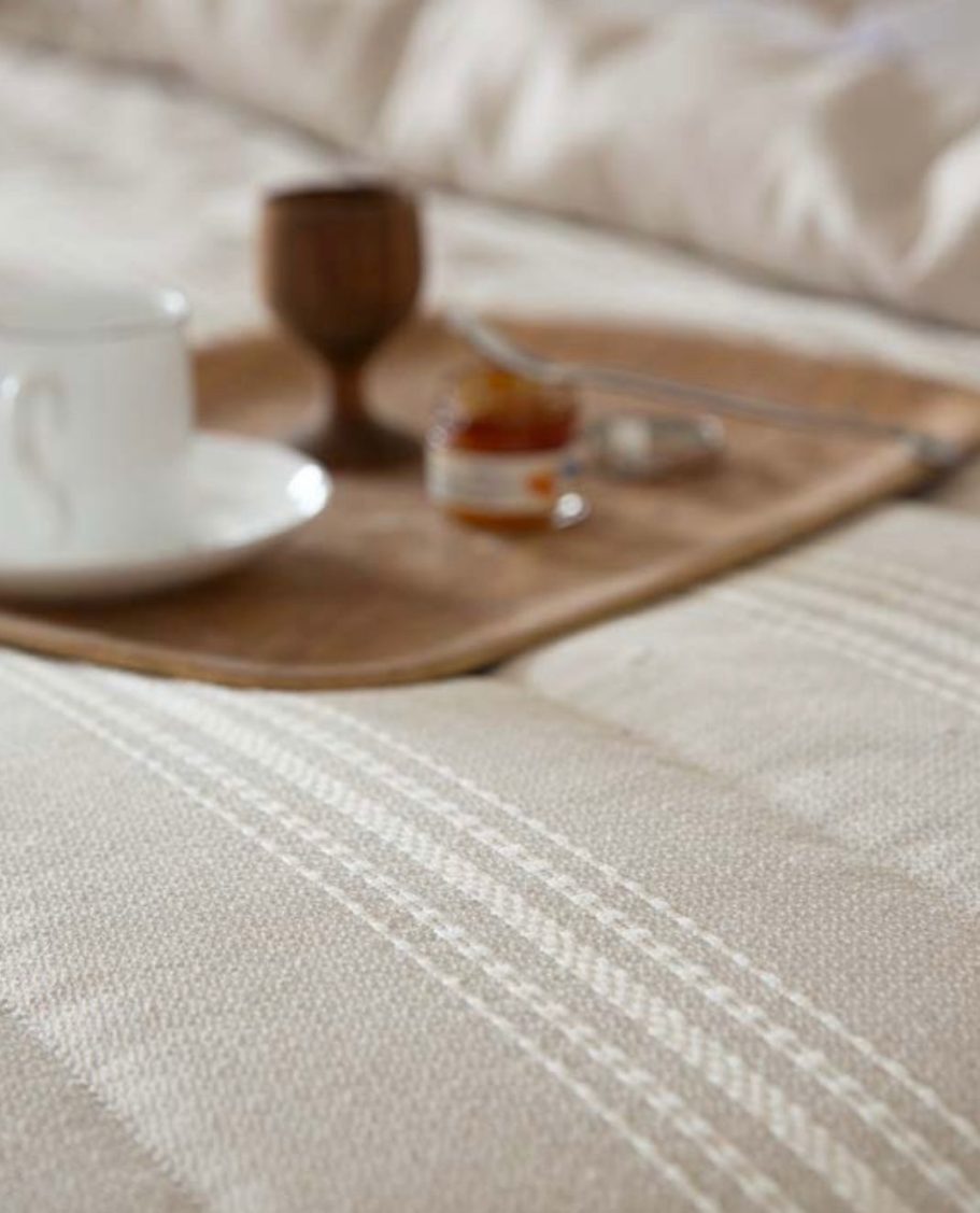 Taza blanca, recipiente de madera y mermelada sobre una bandeja en una cama.