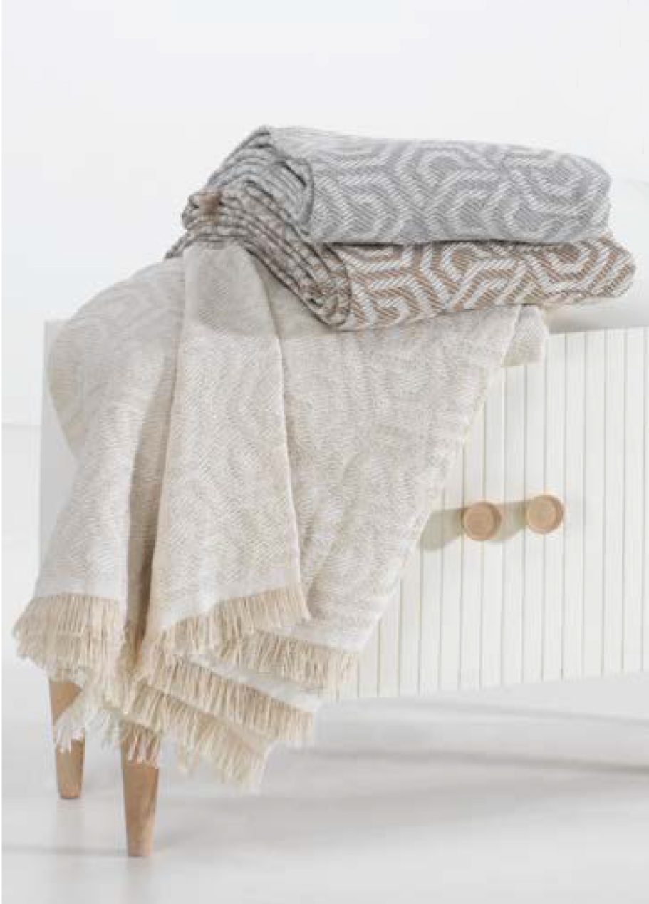 Multiusos de algodón Mantas de diferentes colores con patrones geométricos, apiladas sobre una mesa blanca.