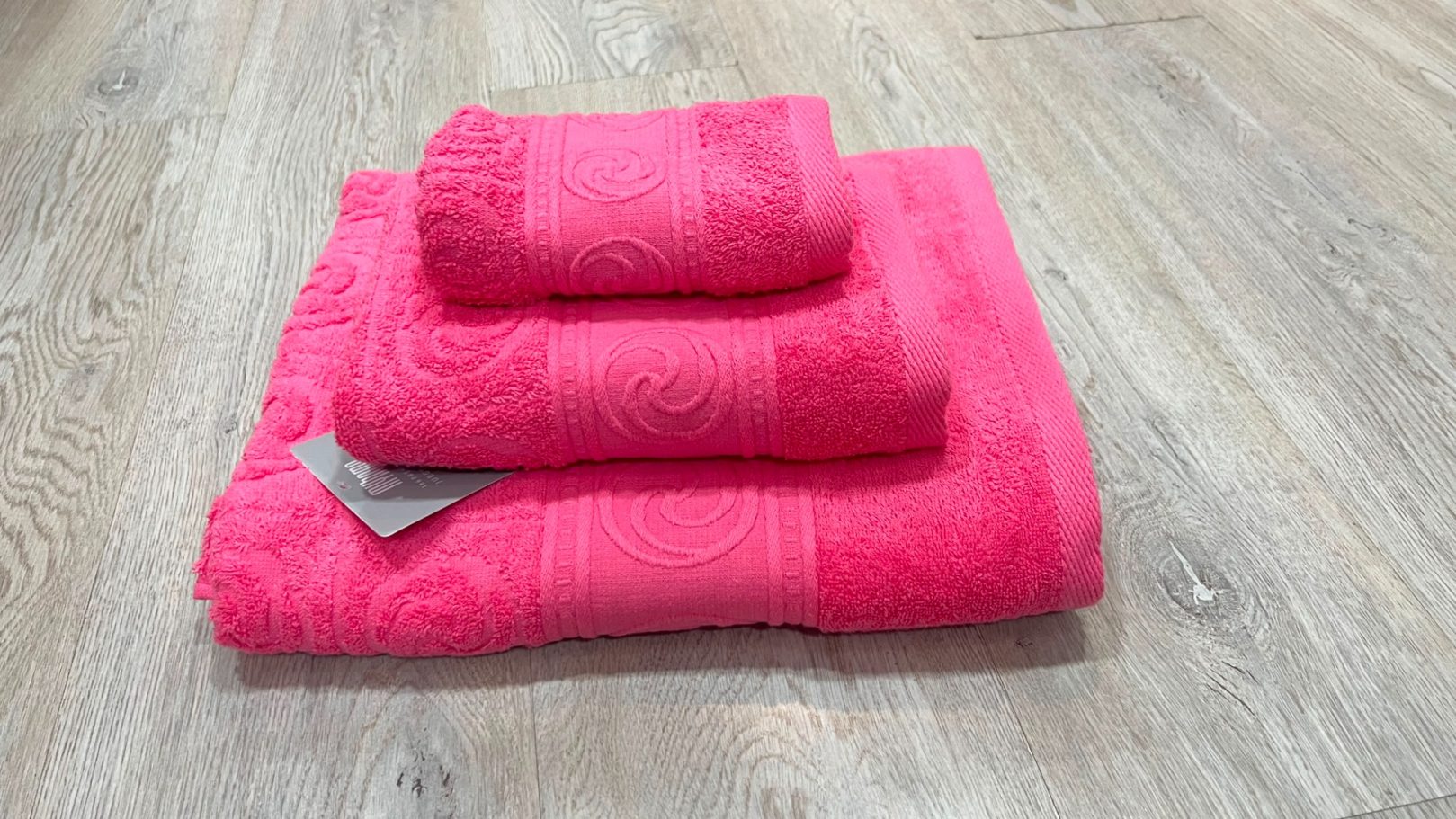 Toallas de color rosa en diferentes tamaños apiladas sobre una superficie de madera clara.